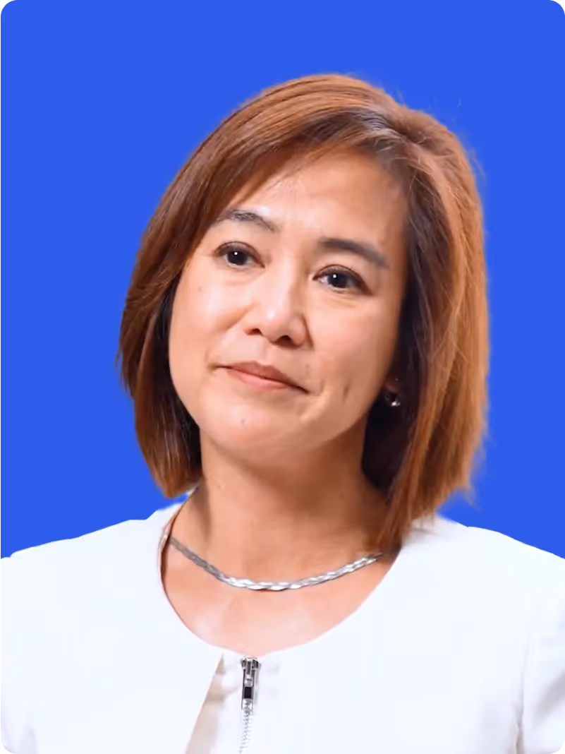 Portrait of a middle-aged woman with light brown hair wearing a white jacket and silver necklace against a blue background.
